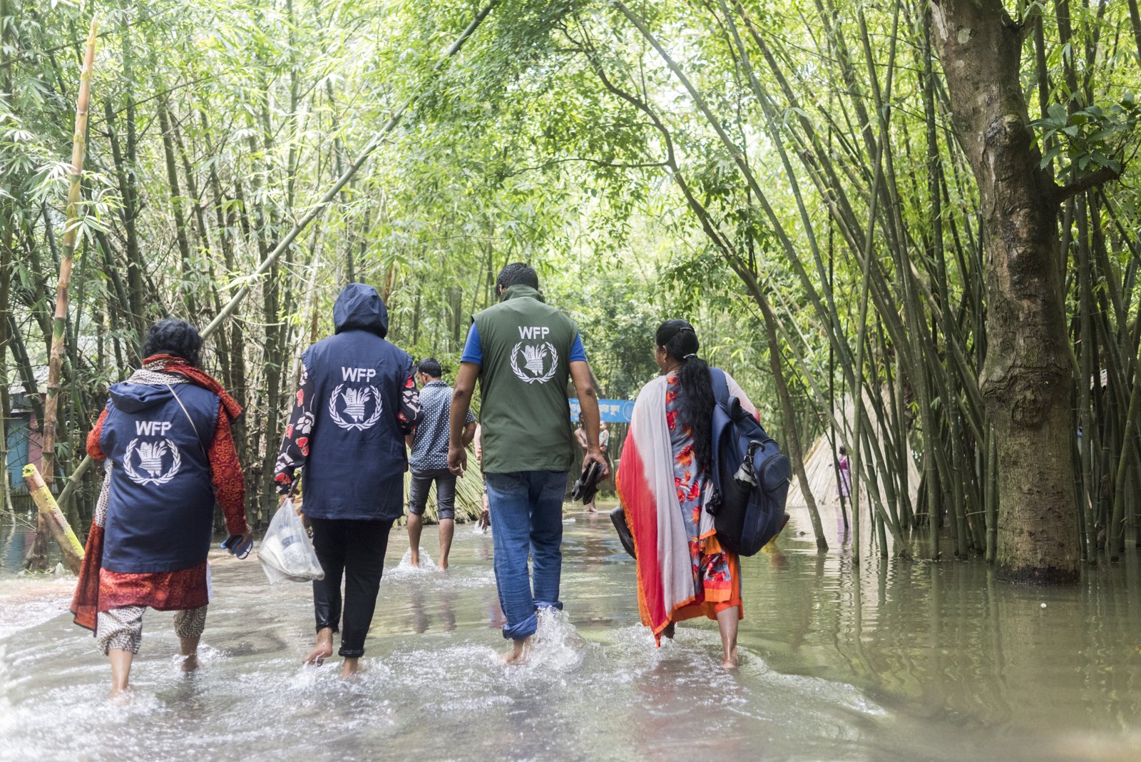 WFP staff and villagers wading barefoot through floodwater in Bangladesh